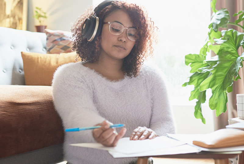 young woman listening to music with headphones, wearing glasses while writing